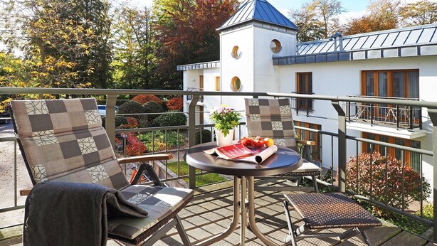 Un balcon avec deux chaises, une petite table et un pot de fleurs.
