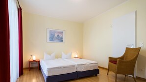 Une chambre à coucher avec un lit double, des lampes de chevet, un fauteuil en osier et un tableau au mur.