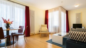 Une chambre d’hôtel moderne dotée d’un coin repas, d’un canapé, d’une télévision et d’une fenêtre avec des rideaux.