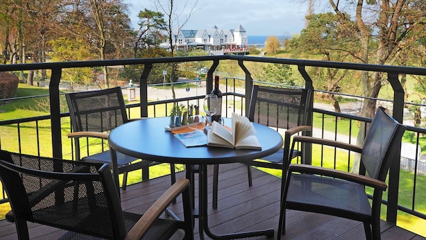 A round table with chairs on an outdoor deck, overlooking a scenic view of trees and a distant building. - Appartement mit 2 Schlafzimmern und Balkon (Seebad Heringsdorf)