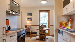 A compact kitchen with a built-in oven, a coffee machine, and a dining area with a table and chairs. - Appartement mit 2 Schlafzimmern und Balkon (Seebad Heringsdorf)