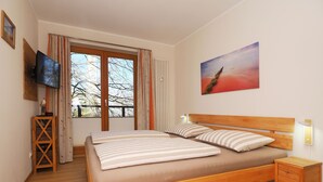 A bedroom with a wooden bed, a nightstand, a TV, and a window with curtains. - Appartement mit 2 Schlafzimmern und Balkon (Seebad Heringsdorf)
