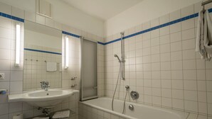 Et badeværelse med vask, spejl, bruser og badekar.