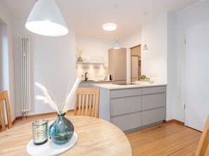 Une cuisine moderne avec des meubles blancs, un îlot central, des luminaires suspendus et un coin repas comprenant une table et des chaises en bois.