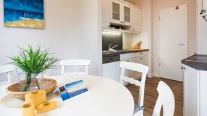 Moderni keittiö, jossa on valkoiset kaapit, musta työtaso ja puulattia. Keittiössä on ruokapöytä tuoleineen, sekä pöydällä kasvi ja esite.