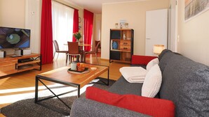 Un salon moderne avec un téléviseur à écran plat, une table basse en bois, un canapé gris et des touches de couleur rouge.