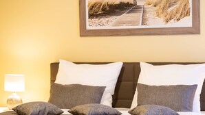 Une chambre à coucher avec un lit, des oreillers, une table de chevet, une lampe et un tableau encadré au mur.