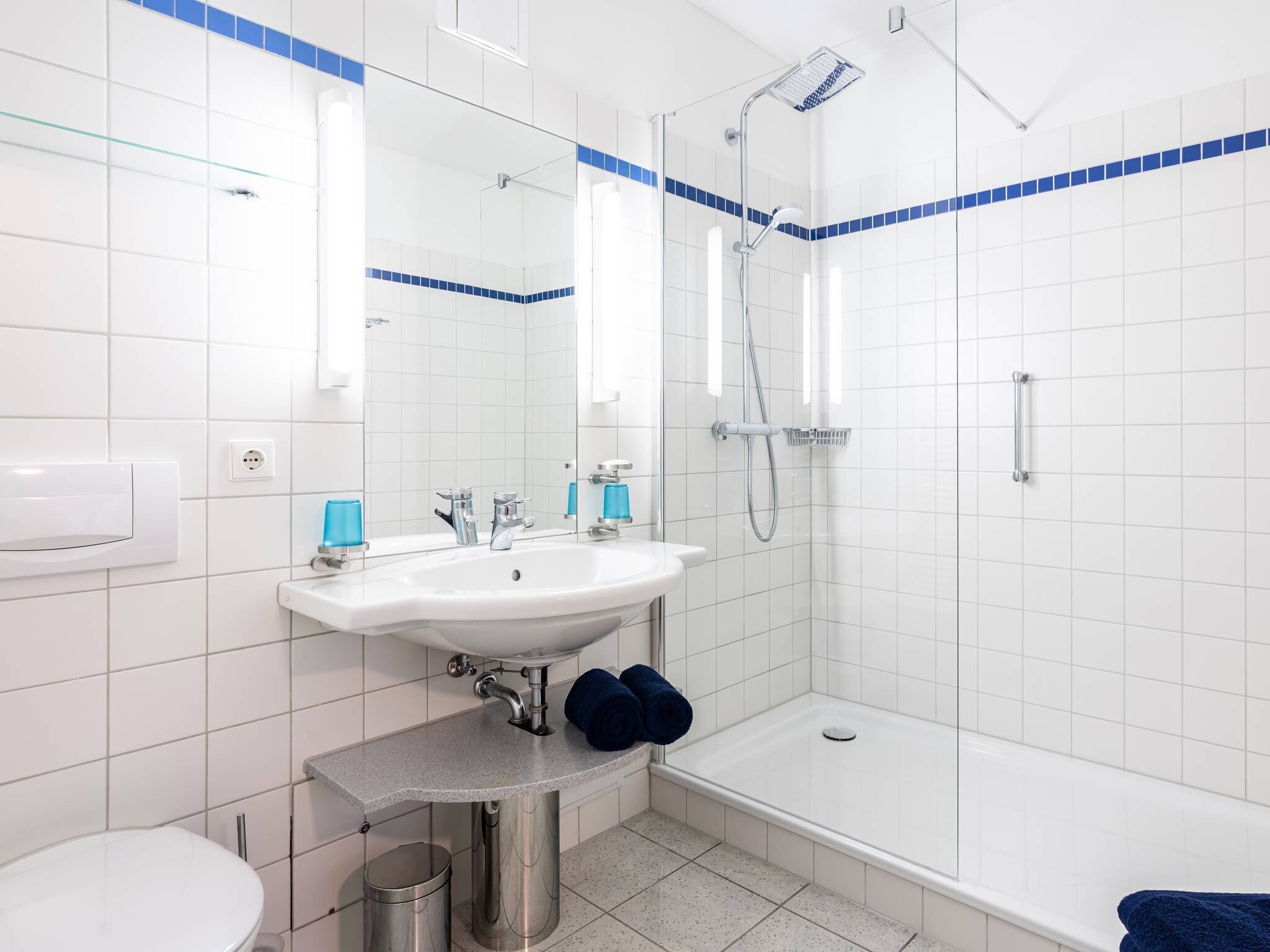 Un baño moderno con un lavabo blanco, dos grifos, un espejo, una ducha y un inodoro.