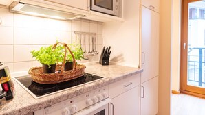 Une cuisine avec des meubles blancs, un four à micro-ondes, une cuisinière et un panier rempli de plantes.
