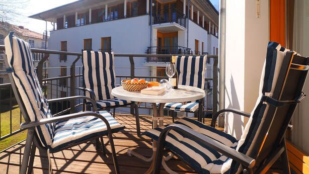 Un balcon avec des chaises à rayures et une table, une bouteille de champagne et un panier d’oranges.