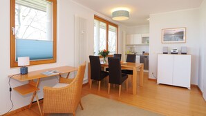 A modern kitchen with white cabinets, a dining area with a wooden table and chairs, and a view of the sea through large windows. - Apartment with 1 bedroom and balcony (Seebad Heringsdorf)