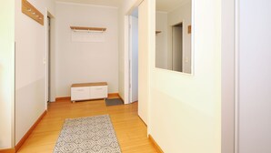 A narrow hallway with wooden flooring, a patterned rug, a white cabinet, and a mirror on the right wall. - Apartment with 1 bedroom and balcony (Seebad Heringsdorf)