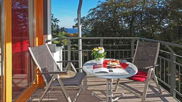 A balcony with a table set for two, featuring a book, a vase with flowers, and a plate of food. - Apartment with 1 bedroom and balcony (Seebad Heringsdorf)
