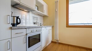 A modern kitchen with white cabinetry, a built-in oven, and a window with blinds. - Apartment with 1 bedroom and balcony (Seebad Heringsdorf)