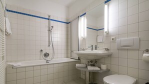 A bathroom with white tiled walls, a bathtub, a sink, a toilet, and a trash can. - Apartment with 1 bedroom and balcony (Seebad Heringsdorf)