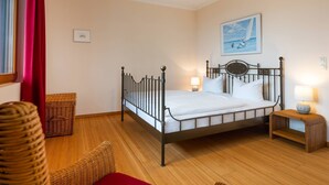 A neatly arranged bedroom with a metal-framed bed, two bedside tables with lamps, wicker furniture, and a painting on the wall. - Apartment with 1 bedroom and balcony (Seebad Heringsdorf)