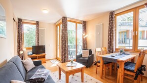 Uma sala de estar aconchegante com sofá, televisão, mesa de jantar com cadeiras e janelas amplas com cortinas.