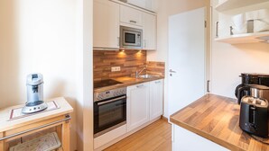 Uma cozinha compacta com armários brancos, micro-ondas, forno, pia e máquina de café.