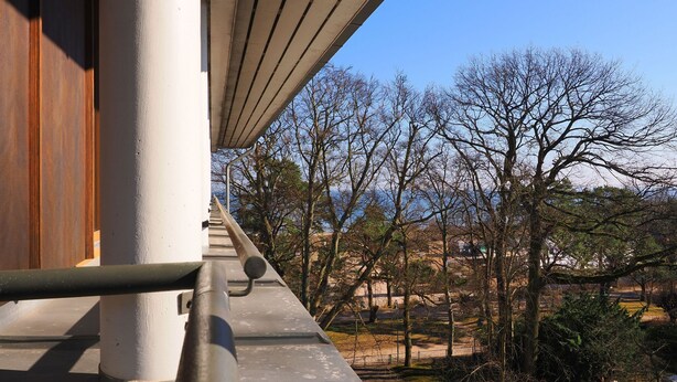 Vista de uma varanda com vista para um parque, árvores e um edifício ao longe.
