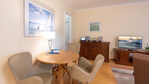Ett modernt vardagsrum med ett runt träbord, två beige fåtöljer, en tv och ett skåp med högtalare.