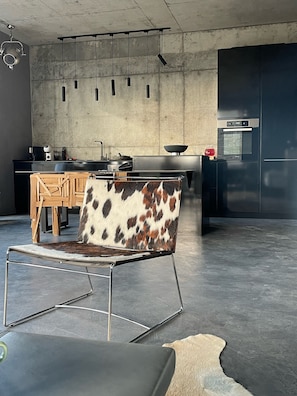 A modern kitchen with a concrete backsplash, stainless steel appliances, and a hanging light fixture.