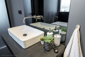 A modern bathroom with a large white sink, a mirror, and a window.
