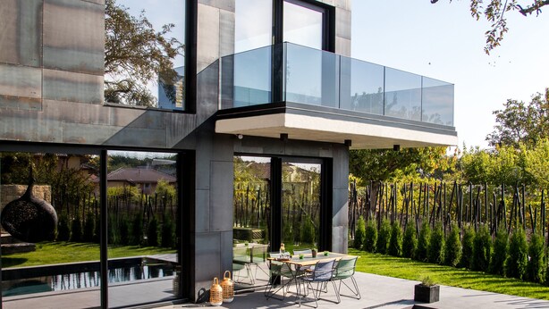 Una casa moderna con un balcón de vidrio que da a una piscina y jardín.