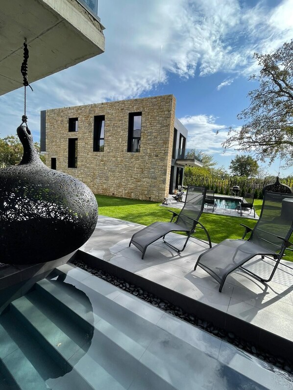 A modern outdoor area with a stone building, a decorative black sculpture, and a pool with lounge chairs.