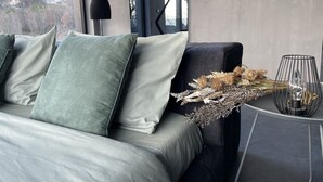 Una sala de estar moderna con un sofá gris, cojines verdes y una mesita de noche con flores secas y una lámpara.