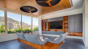 A modern living room with a large window, built-in entertainment unit, and a wooden ceiling fan.