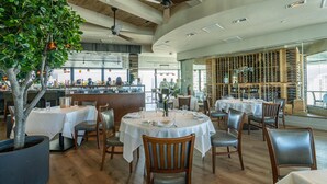 Ein Restaurant mit runden Tischen, Holzstühlen und einem großen Topfbaum.