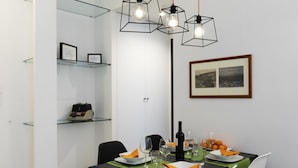 Comedor con estante de vidrio, cuadros enmarcados y una mesa preparada para cuatro, con platos, vasos y una botella.