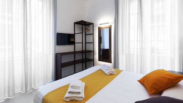 Una habitación de hotel con cama, televisión montada en la pared, armario y espejo.