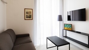 Una sala de estar moderna con un sofá, una mesita, un televisor montado en la pared y un marco de fotos en un estante.