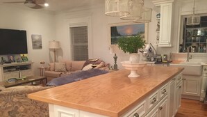 A modern kitchen with white cabinetry, a wooden island, and a dining area with a sofa and coffee table. - Crisp and clean beach block home (monterey beach)