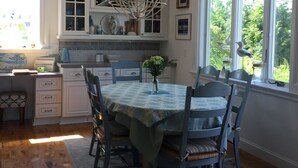 A kitchen with white cabinets, a dining table with chairs, a chandelier, and a window with a view of greenery. - Crisp and clean beach block home (monterey beach)