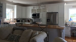 A modern kitchen with white cabinetry, stainless steel appliances, and a wooden island. - Crisp and clean beach block home (monterey beach)