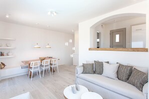 A modern living room with a sofa, a dining area with a table and chairs, and a large mirror on the wall.
