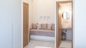 Quarto compacto com um banco embutido, um espelho redondo e uma mesa de cabeceira com pia.