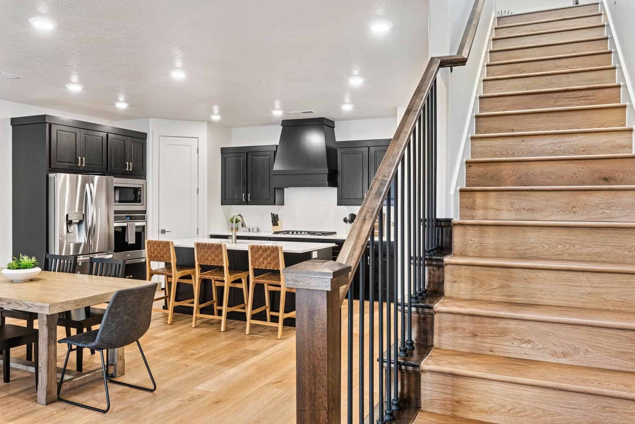 Une cuisine moderne avec des meubles de couleur sombre, des appareils électroménagers en acier inoxydable et un escalier en bois.