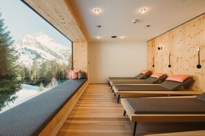 A room with wooden floors, a large window with a view of mountains, and several beds with pillows. - Alpin - Studios & Suites (Warth)