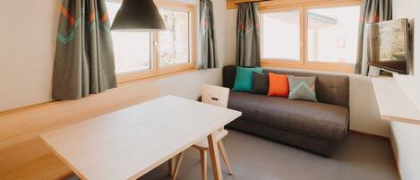 Et moderne interiør med træloft, en sofa med farverige puder, et spisebord og et fjernsyn på væggen.