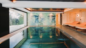 Una piscina interior moderna amb parets de vidre transparent, revestiment de fusta i un mural de muntanyes.