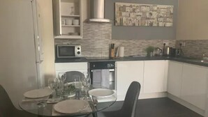 A modern kitchen with white cabinets, a microwave, and a gas stove. There is a dining table with chairs and a glass top. - Sherwood-free Parking-business-leisure (Nottingham)