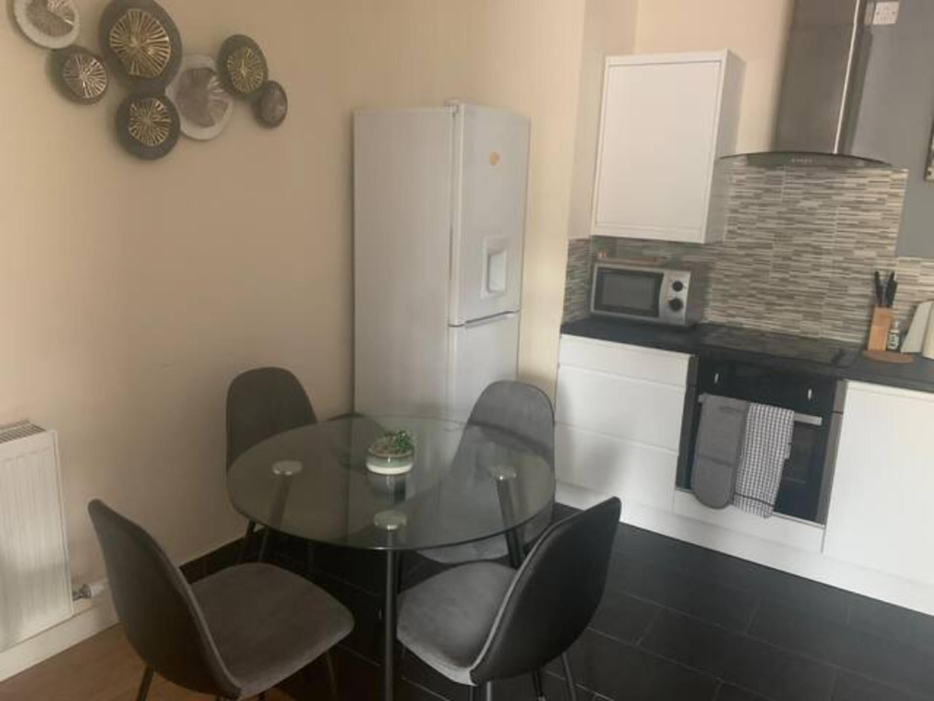 A compact kitchen with a microwave, refrigerator, and a small dining area with a glass table and four chairs.