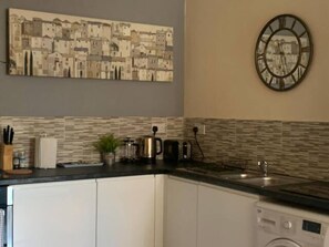 A kitchen with white cabinets, a tiled backsplash, a clock, and a coffee maker. - Sherwood-free Parking-business-leisure (Nottingham)