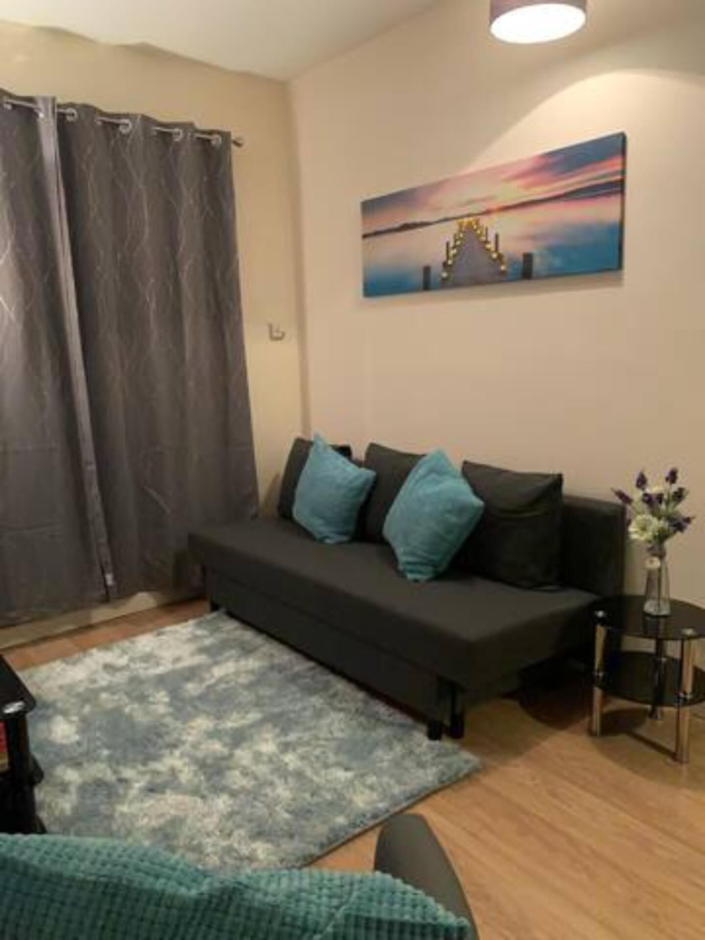 A living room with a dark sofa, a blue rug, and a painting on the wall.