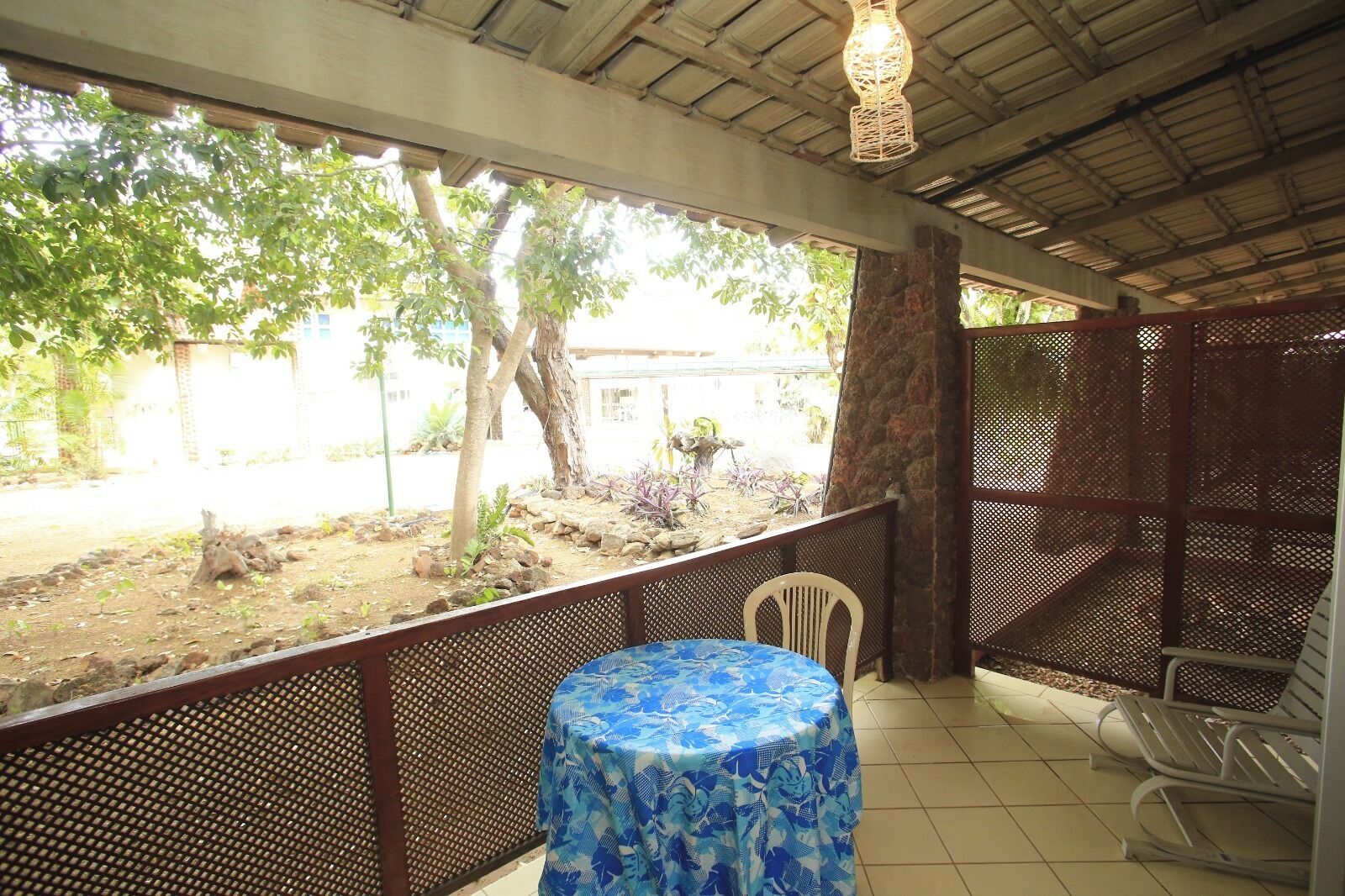 A covered outdoor seating area with a table and chairs, a view of trees and a building in the background.