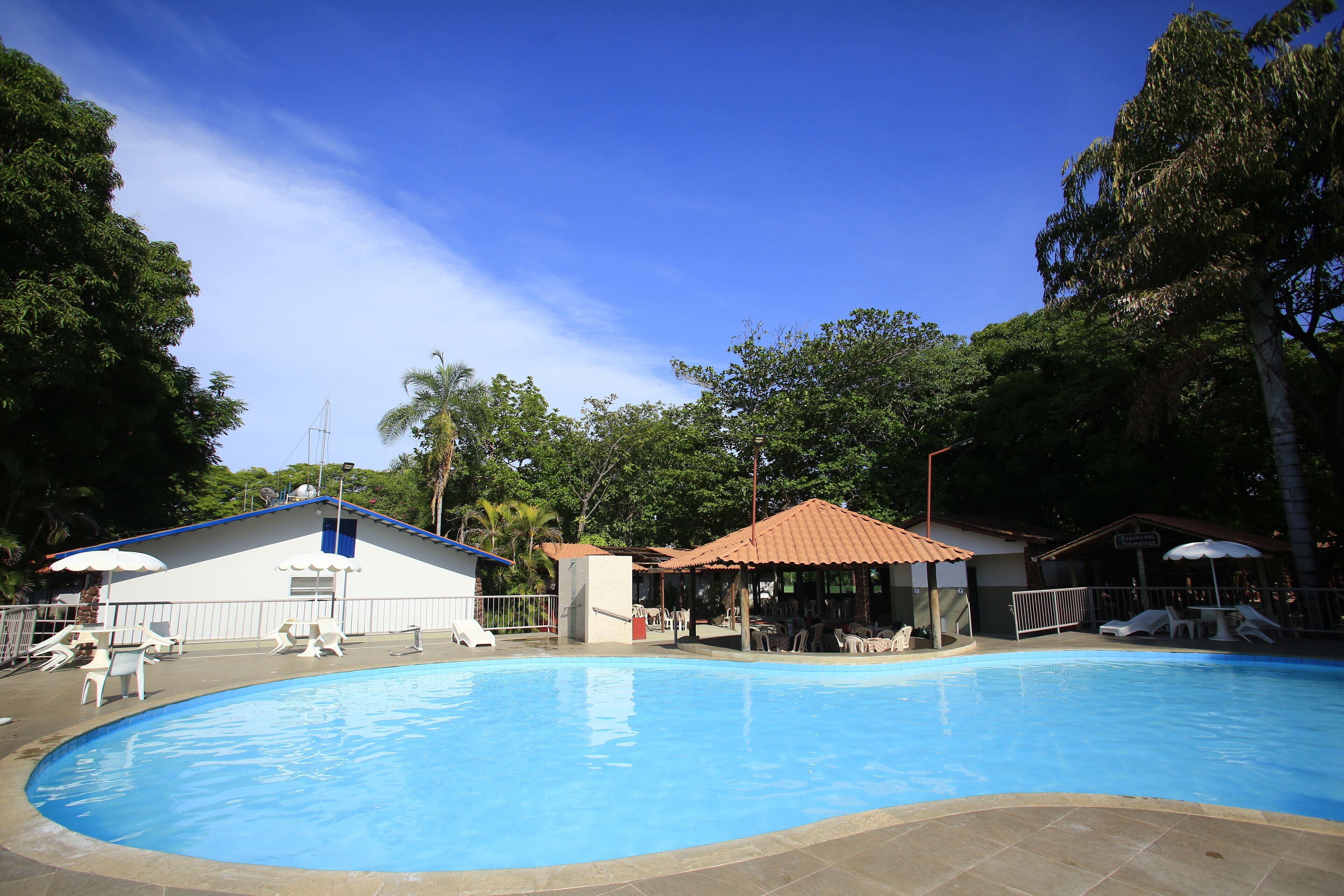 A swimming pool with lounge chairs and umbrellas, surrounded by trees and buildings with red-tiled roofs.