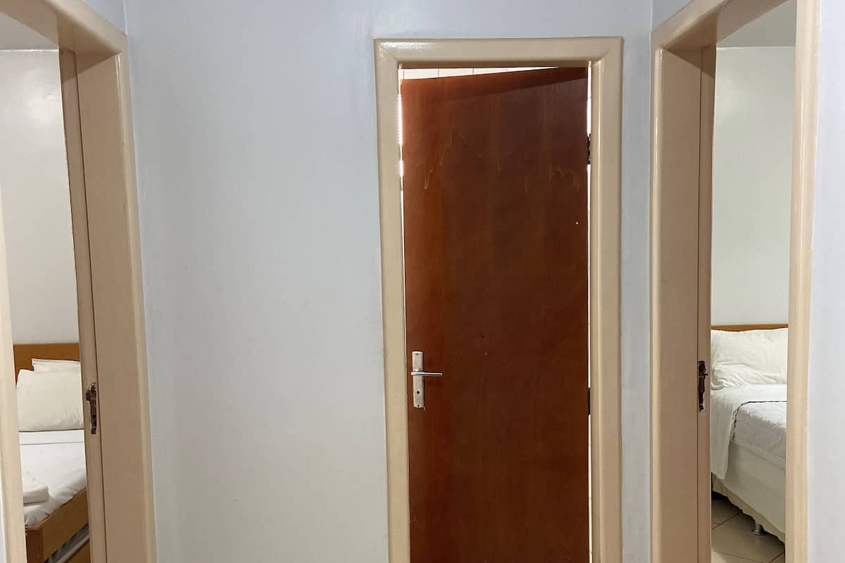 Una habitación con puerta de madera, paredes blancas, una cama con ropa de cama blanca y una alfombra pequeña en el suelo.